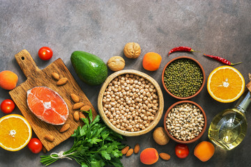 Set uncooked healthy balanced food, salmon,legumes, fruits, vegetables, olive oil and nuts, dark rustic background. Overhead view, flat lay,border.