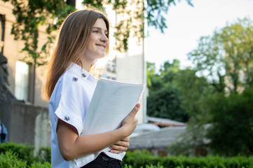 Fototapeta premium student standing near the university, holding papers in her hands and smiling against the background of the college, she goes to school