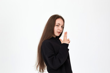 Young pretty brunette woman wears black sweatshirt and stands over white background. Girl holds imaginable gun in her hands.