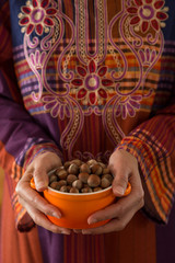 the woman wearing traditional clothes holds hazelnuts in the bowl.