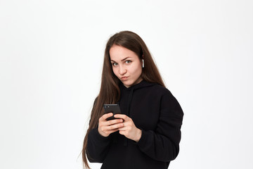 Studio shot of a beautiful young brunette woman with wireless headset and phone looking intrigued at the camera while standing over white background.