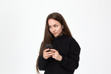 Studio shot of a beautiful young brunette woman with wireless headset and phone looking intrigued at the right side while standing over white background.