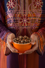 the woman wearing traditional clothes holds hazelnuts in the bowl.