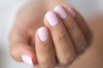Close-up photo of elegant light pink manicure over white shirt background, tender women's hands...