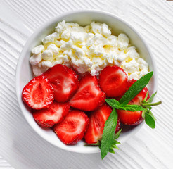 White bowl with fresh red ripe strawberries and natural cottage cheese