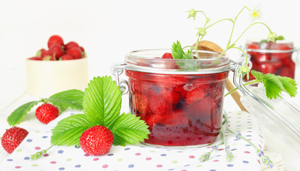 Delicious strawberry jam in traditional glass jar on white wooden background