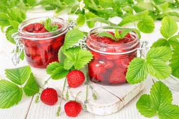 Delicious strawberry jam in traditional glass jar on white wooden background