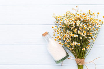 Sea salt, aromatherapy oil in bottles and chamomile on vintage wooden background.