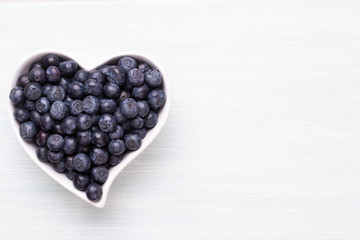 Fresh blueberries, in a heart shaped bowl on a wooden background.