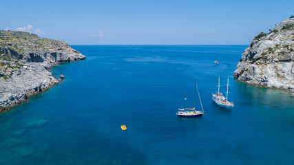 Fototapeta na wymiar Sailing boats at the beautiful Blue Lagoon at Rhodes Island with blue clear sea water, blue sky and rocks in the water