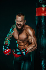 Sportsman with tattoos, man boxer fighting in gloves with boxing punching bag. Isolated on black...
