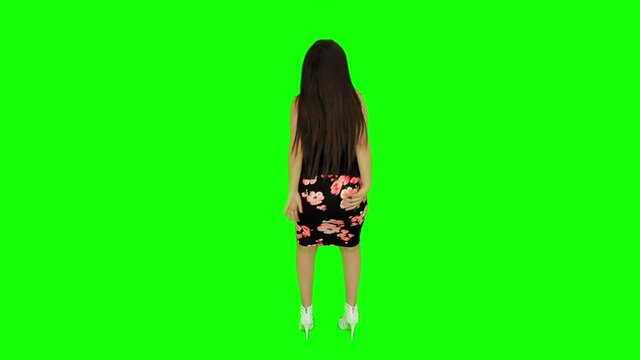 Sexy woman Model with sexy ass dancing back and shaking ass in front of a green screen with flower dress, white high heels and black top. Static Wide shot. 4K.