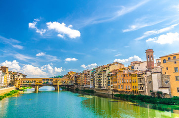 Ponte Vecchio stone bridge with colourful buildings houses over Arno River blue turquoise water and embankment promenade in historical centre of Florence city, blue sky white clouds, Tuscany, Italy