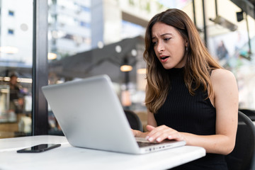 Business woman work process concept. Shocked female freelancer stares at laptop computer with...