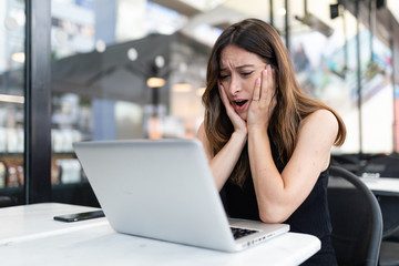 Business woman work process concept. Shocked female freelancer stares at laptop computer with bugged eyes, Blurred background, film effect.