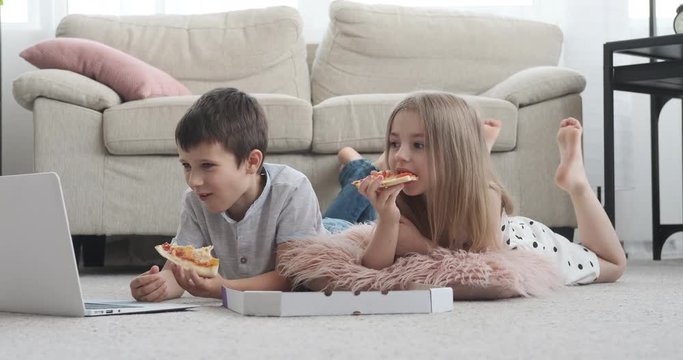 Little brother and sister enjoying movie on laptop while having pizza at home