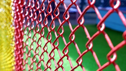 Fototapeta premium Side view and selective focus of colorful wire mesh fence with sunlight and shadow on green atrificial grass floor in playground area at kidergarten school