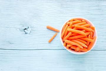 Baby carrot healthy salad is in a thin white bowl on a blue wooden floor from the top view