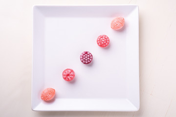 Five candy canes sweets in form of juicy berries on white plate on white background isolated top view