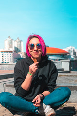 woman with pink hair in sunglasses smiling while eating wafer roll