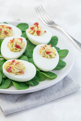 Deviled eggs stuffed with avocado, egg yolk and mayonnaise filling garnished with bacon on spinach leaves, vertical