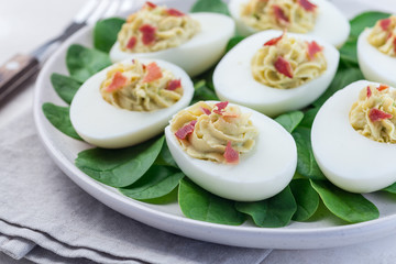Fototapeta na wymiar Deviled eggs stuffed with avocado, egg yolk and mayonnaise filling, garnished with bacon on spinach leaves horizontal