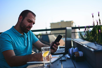 Concentrated pensive young handsome man  sitting in cafe, thinking and using laptop. Outdoor cafe.