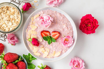 overnight oats or oatmeal porridge with fresh strawberries, almonds and mint in a bowl with rose flowers