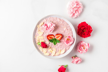 romantic healthy breakfast. bowl of overnight strawberry oats with fresh berries, almonds and mint with rose flowers