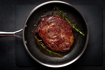 Grilled premium rib eye beef steak in the pan, cooking steak in the kitchen on a dark background,...