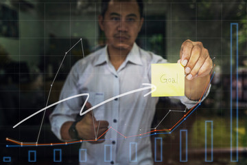 Motivation, Aim, Traget and Goal Concept. Businessman holding sticky note with "goal" word and graph report on glass window.