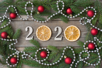 Fototapeta na wymiar 2020 New year rustic background with orange slices, fir tree branches, red baubles and bead chain on wooden boards