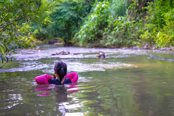 little asian girl wearing inflatable sleeves swimming in nature water on holiday