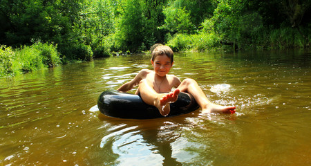 The boy has fun on an inflatable tubing in the river.