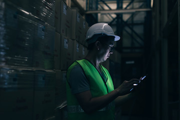 Side view of Asian young warehouse worker man with safety hard hat is checking order details with a...