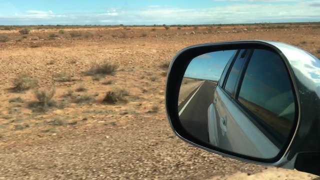 Reflection of Stuart Highway road and central Australia Outback landscape as view from a car wing mirror during a rod trip in the red center of Australia.