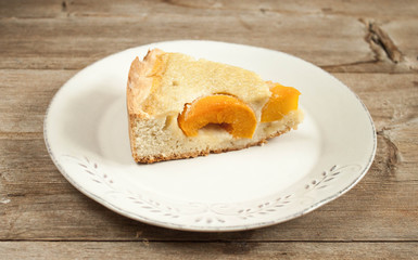 Slice of open peach apricot pie on white plate on wooden table horizontal macro close-up.