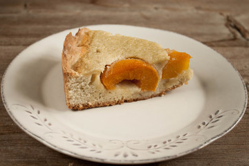 Slice of open peach apricot pie on white plate on wooden table horizontal macro close-up.