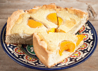Slices of peach apricot pie or cheese cake on bright oriental plate on wooden table background