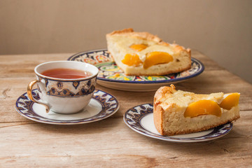 Slice of peach apricot pie or cheese sour cream cake on bright saucer with tea cup on wooden table