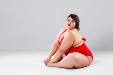Plus size model in red lingerie, fat woman in underwear on gray background, body positive concept
