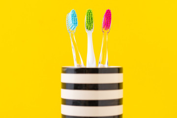 Three plastic colorful toothbrushes in glass on a yellow background, close up
