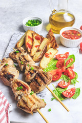 Grilled chicken skewers with baked potato, green onion and salsa sauce on a marble plate on a light gray background. Selective focus