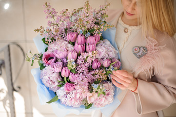 Girl in the coat looking at the bouquet of purple violet tulips and lilac