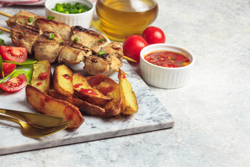 Grilled chicken skewers with baked potato, green onion and salsa sauce on a marble plate on a light gray background. Selective focus