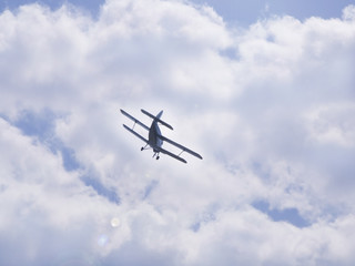 Fototapeta na wymiar Flying light aircraft blue on a background of white clouds. Bottom view of airplane silhouette