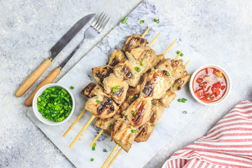 Grilled chicken skewers with green onion and salsa sauce on a marble plate on a light gray background. Top view.