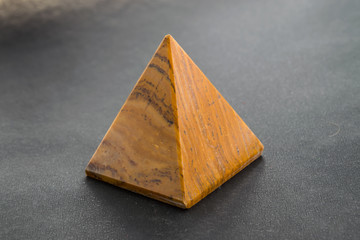 Tiger eye stone in the shape of a pyramid close-up on a black background for jewelry