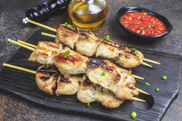 Grilled chicken skewers with green onion and salsa sauce in a cutting board on a dark background. Selective focus