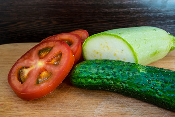 Three cloves of garlic, cucumber and tomato rings on a cutting board and parsley greens with zucchini